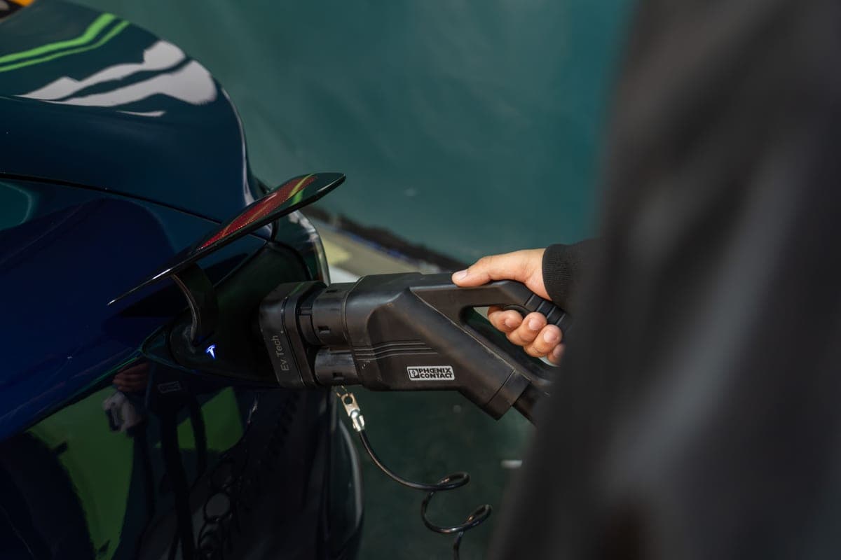 A person plugging a charging cable into an electric car outside a house
